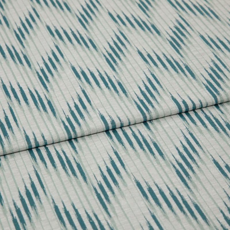 Folded woven fabric with teal ikat-like diagonal stripes and subtle vertical ribbing — folded once, lying flat on a neutral surface, close-up, soft even lighting.