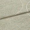 Woven upholstery fabric with small grid and concentric circular motif, folded to show layered edge and textured weave, close-up on a flat surface under soft, neutral lighting.