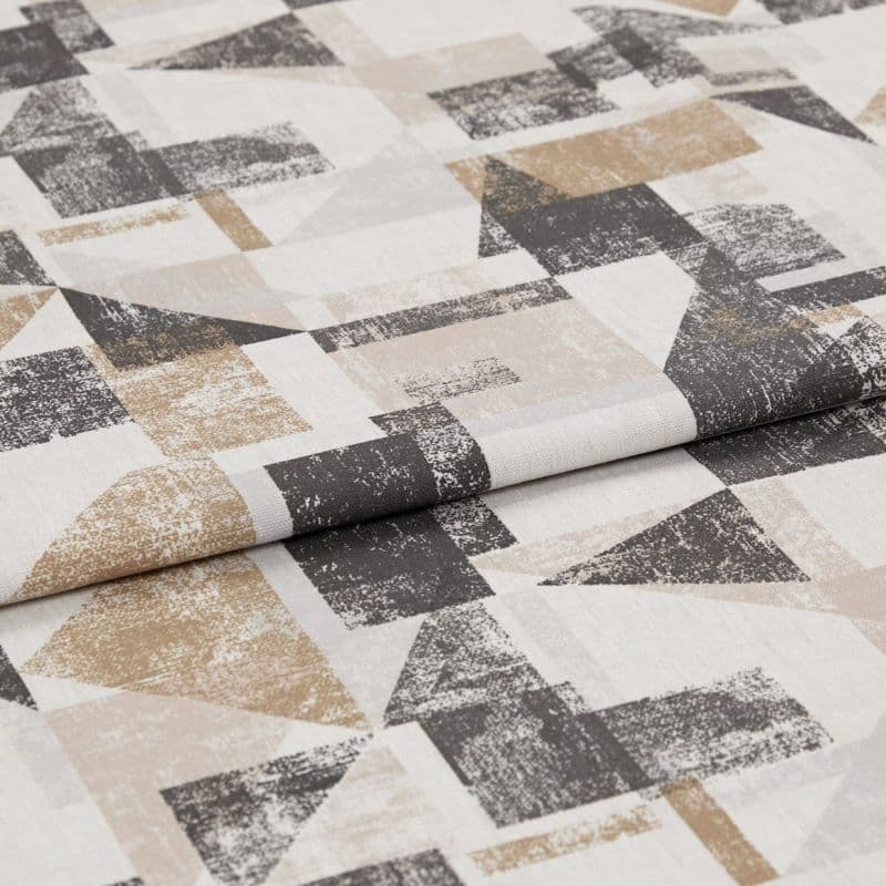 Folded textile sample with distressed geometric print—overlapping triangles and rectangles in beige, tan and charcoal on off-white—laid flat with a visible central fold under soft studio lighting.
