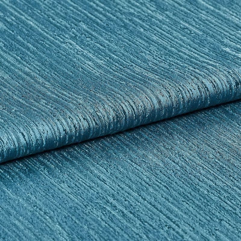 Teal ribbed fabric (folded), showing horizontal raised ridges and woven sheen; folded layers lie against each other in a close-up studio shot with even lighting, emphasizing texture and subtle metallic shimmer.