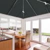 Dark gray pleated blinds on the pitched ceiling and white pleated blinds on windows and doors, lowered and filtering light; bright kitchen-dining area with wooden table, beige chairs, patio view.