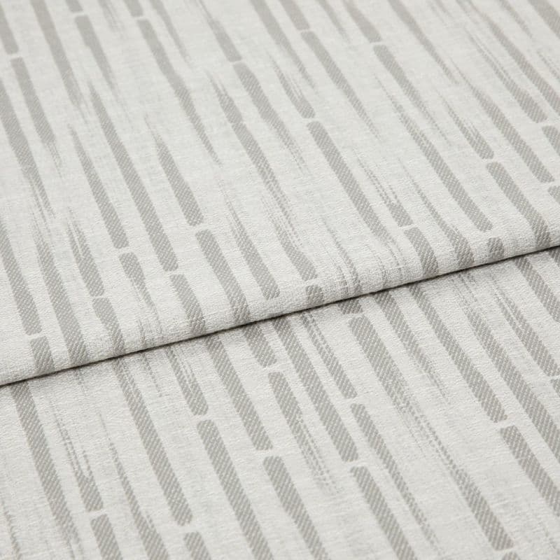 Light-gray patterned fabric, folded in overlapping panels, displaying vertical rounded dashes; close-up on textured linen-like material under soft, even lighting.