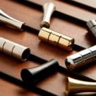 Polished cylindrical metal beads (gold, silver, black) strung on parallel dark rods, sliding along them; set on a warm wooden board under soft directional lighting with shallow focus.