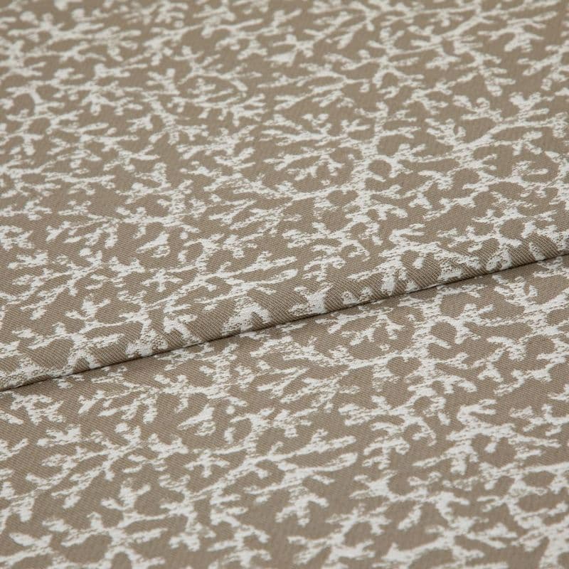 Beige woven fabric with a white, branch-like pattern folded across itself, shown close-up on a flat surface under soft, even lighting.