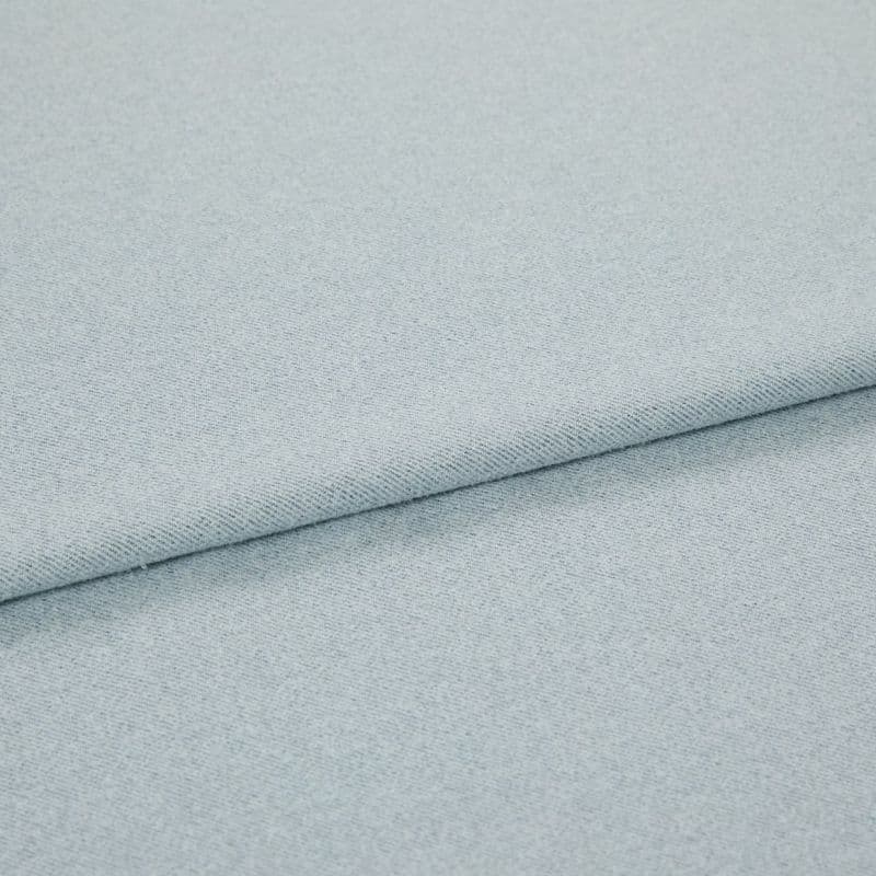 Pale blue woven fabric folded into overlapping layers; diagonal fold runs across frame, showing fine twill-like weave and subtle speckling under soft, even studio lighting.