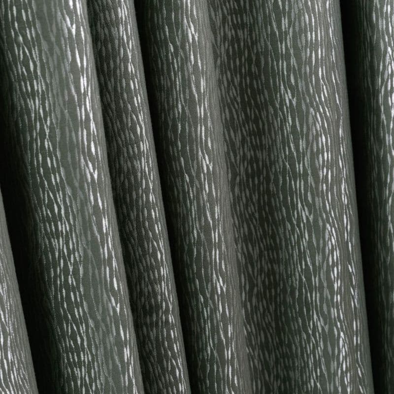 Heavy dark green patterned curtains with vertical folds and subtle silver streaks, closed and hanging in tight pleats, indoors under soft light, close-up with no visible view.