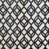 A beige rectangular rug with bold navy geometric diamond-lattice pattern lies flat (object), displayed as a close-up sample (action) under neutral studio lighting with no surrounding room visible (context).