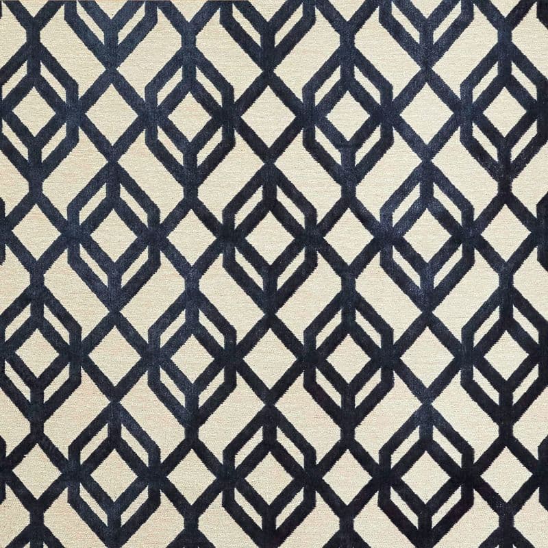 A beige rectangular rug with bold navy geometric diamond-lattice pattern lies flat (object), displayed as a close-up sample (action) under neutral studio lighting with no surrounding room visible (context).