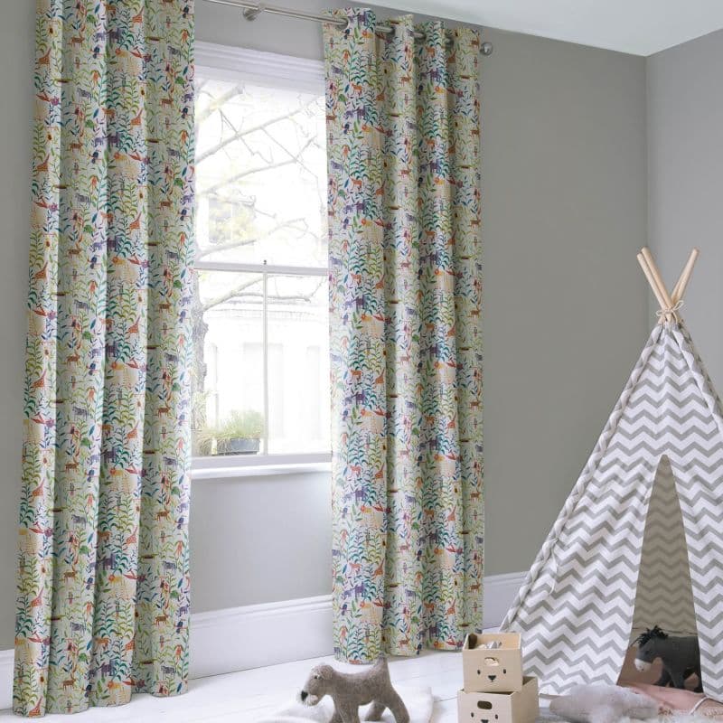 Grommet-top curtains with colorful animal-and-foliage print, hung each side of a sash window on a rod, framing and filtering daylight in a pale-gray children's playroom with a chevron teepee.