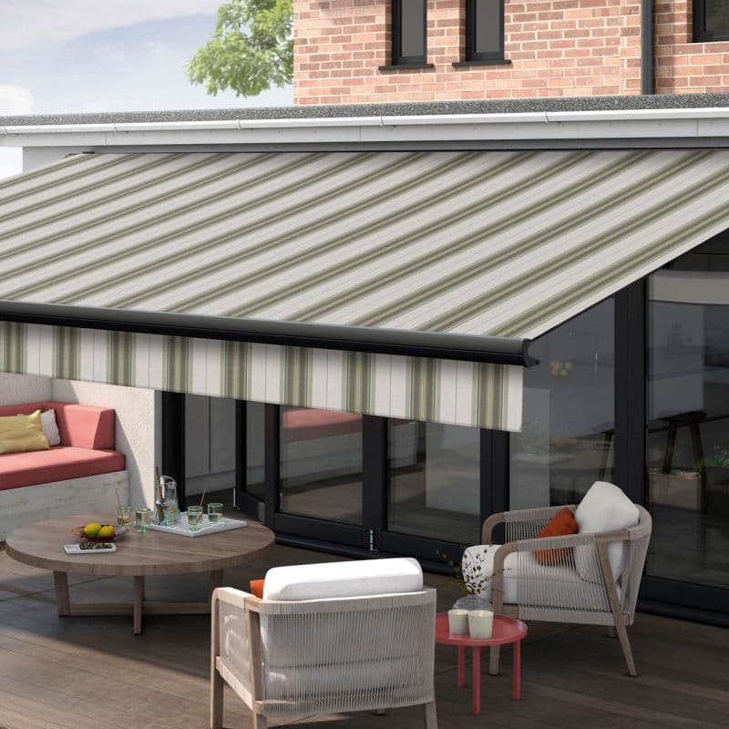 Striped fabric retractable awning, green-and-cream diagonal stripes, fully extended over glass patio doors; shading an outdoor lounge with wicker armchairs, low wooden table, cushioned bench, and daylight.