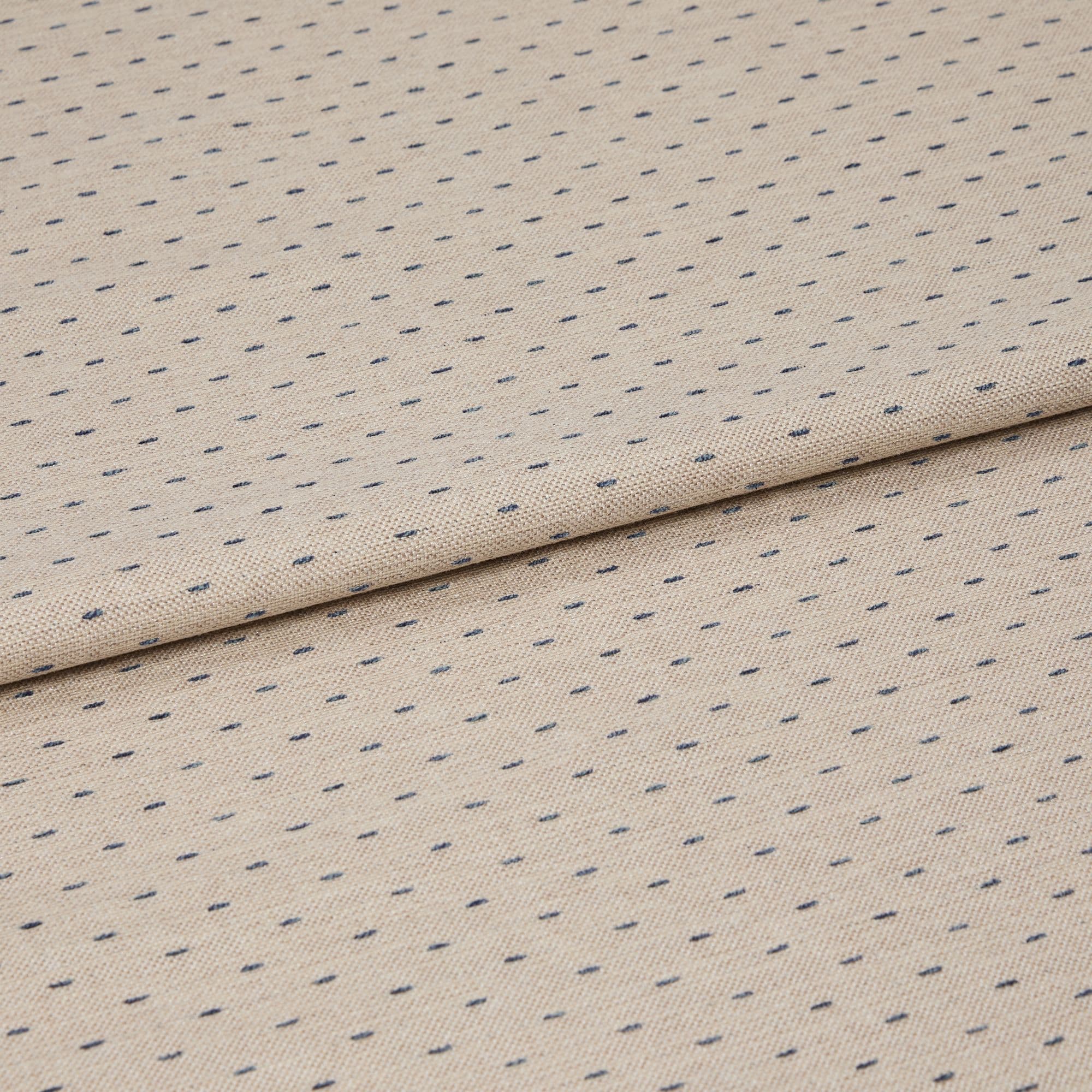 Beige woven fabric with regular small navy dash dots, folded once across center, lying flat on a neutral surface; close-up, even studio lighting highlighting its textured weave.