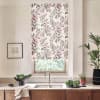 Patterned roller blind with pink and gray leaf motif covers a window above a stainless faucet and double sink, set in a bright kitchen with wooden cabinets, plants, decor.