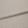 Beige jacquard-like upholstery fabric, folded over itself, displaying a dense small pebble motif; close-up studio-lit view highlighting subtle sheen, woven texture, and gentle drape.