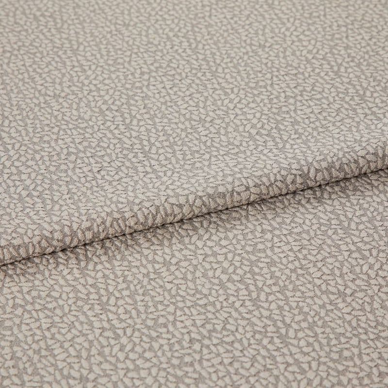 Beige jacquard-like upholstery fabric, folded over itself, displaying a dense small pebble motif; close-up studio-lit view highlighting subtle sheen, woven texture, and gentle drape.