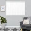White vertical blinds, closed—evenly spaced slats with scalloped weighted bottoms—filtering bright daylight; mounted in a gray-walled living room above a patterned rug, beside a potted plant and gray armchair.