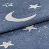 Blue woven curtain fabric printed with white crescent moon and stars, folded over itself with a distressed print, close-up macro view of textured textile under soft, neutral lighting.