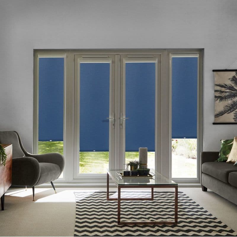Blue roller blinds cover two central French doors and flanking narrow windows, mostly lowered and filtering daylight. Modern living room with glass coffee table, chevron rug, armchairs, and natural light.