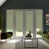 French doors with lowered sage roller blinds block most light, revealing a sliver of garden; a glass coffee table sits on a black-and-white chevron rug between two green armchairs.