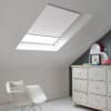 Room with white eaves wall, dark blue-grey wall to right with a shabby chic white drawer unit, a contemporary white chair, white painted floorboards and a skylight blind in lily white.