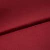 Burgundy satin fabric, folded diagonally with a soft sheen and smooth texture; fold casts a subtle shadow, close-up on a flat surface under even studio lighting.