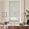 Window with a semi-opaque roller blind, diffusing daylight; positioned above a kitchen sink and faucet, surrounded by countertop with a bowl of greens, potted plants, and framed sketch on wall.