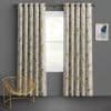 Grommet-top floral curtains, cream with muted beige and yellow blossoms, hang in pleats framing a central window, filtering soft daylight in a gray-walled room with a gold wire chair.