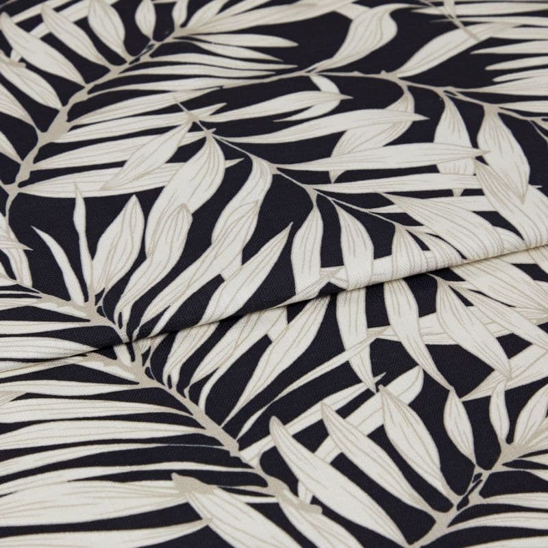 A folded decorative fabric with cream palm-leaf print on a black background; the layers overlap, emphasizing texture and weave, shown in a close-up under soft, even lighting.