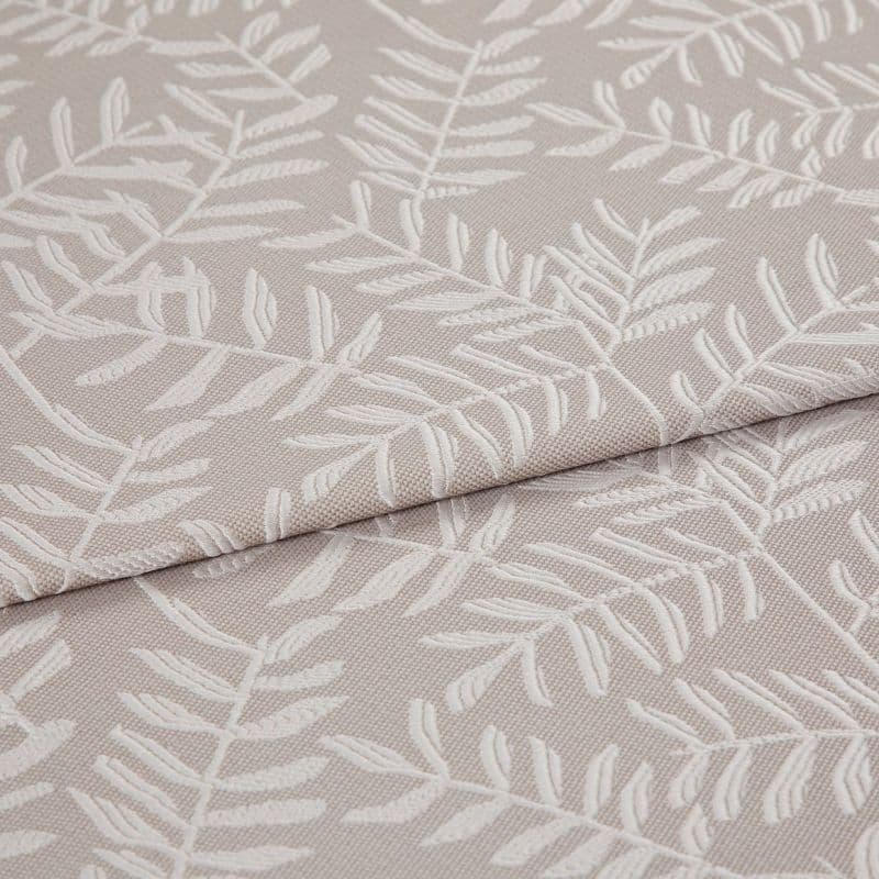 Beige jacquard fabric with raised white fern motif; folded and overlapped; close-up of an upholstery/curtain sample on a flat surface under soft, neutral lighting.