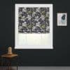 A floral Roman blind, dark background with blossoms and green leaves, is lowered across a white window, softly filtering daylight in dark room with side table and abstract wall art.