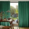 Floor-length, pleated emerald-green curtains hang either side of a patio door, parted to reveal a sunlit backyard; dining table set for breakfast with a pendant lamp in the foreground.