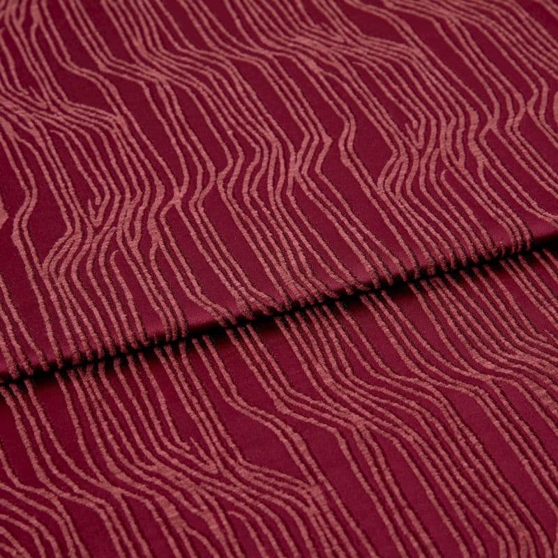 Burgundy fabric with raised, irregular pale-pink wavy lines (textured pile), folded once across the center, lying flat in a close-up, evenly lit studio view, showing pattern and subtle shadows.