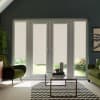 French doors with four glass panels and beige roller blinds partially lowered, letting garden light through, in a modern living room with green chairs, glass coffee table and chevron rug.