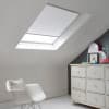 Room with white eaves wall, dark blue-grey wall to right with a shabby chic white drawer unit, a contemporary white chair, white painted floorboards and a skylight blind in white.