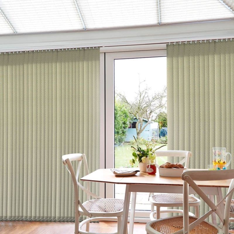 Beige vertical blinds across a sliding glass door, mostly closed with a central garden gap; filtering daylight into a dining nook with wooden table, white chairs, vase.