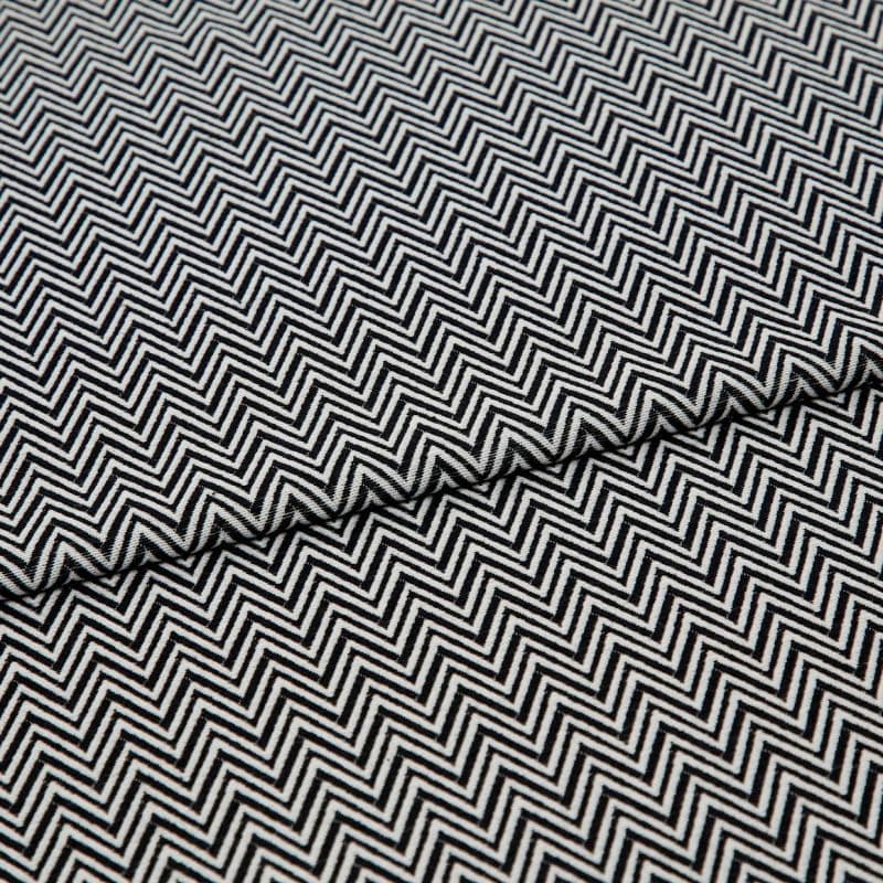 Black-and-white chevron-patterned fabric, folded across the center and showing dense, repeating zigzag lines; lying flat, closely cropped, with even studio lighting highlighting its texture.