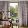 Pleated, floor-length curtains with a purple sprig pattern, hung at a sliding door and drawn apart; framing a sunlit backyard view and a breakfast-set dining table under a pendant light.