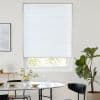 White pleated cellular blind, lowered nearly to the sill with horizontal seams, diffusing daylight; set in a white dining area with marble table, black chairs and a potted fiddle‑leaf fig.