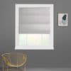 Gray fabric Roman shade lowered partway, smooth folds filtering diffuse daylight through window; white-trimmed opening in a gray wall with gold wire chair and abstract wall art.