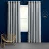 Light-gray grommet-top curtains, hanging in neat pleats on a metal rod, parted to reveal a sunlit window; navy-blue wall, minimalist gold wire chair and circular wall sconce.