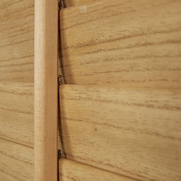 Wooden plantation shutters with a central vertical tilt rod and overlapping horizontal slats — closed, aligned to block light — close-up interior view showing warm wood grain and soft ambient light.