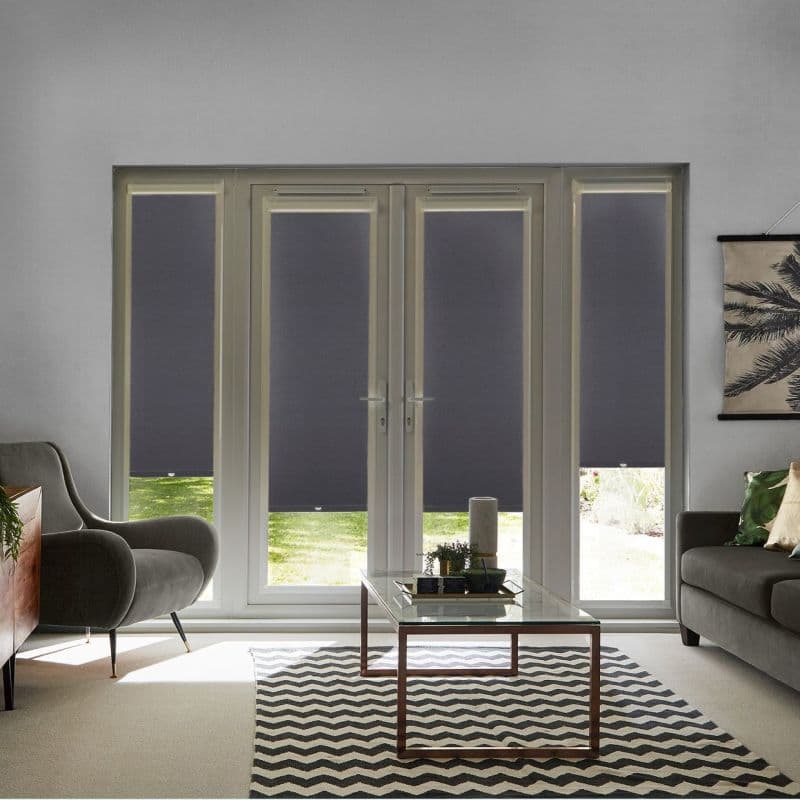 Dark gray roller blinds on four French-door panels and sidelights, lowered to mid-height with small bottom gaps; filtering daylight and blocking view in a living room with sofa, armchair, and glass coffee table.