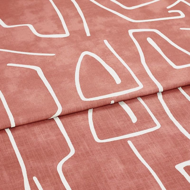 Folded patterned fabric: a rose‑terracotta curtain-like textile with white abstract line motifs, folded once across the frame. Close-up studio view emphasizing soft woven texture and matte finish.