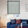 Pleated cellular blind, lowered almost fully with a narrow gap at the bottom and fine horizontal ribs, blocking and softly filtering daylight over a living room with blue sofa, lamp, and artwork.