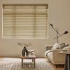 Beige horizontal venetian blinds covering the window, slats mostly closed and filtering soft daylight; above a neutral living room with beige sofa, wooden coffee table and a black floor lamp.