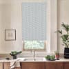A light-gray roller blind patterned with white stars covers a kitchen window above a stainless sink, framed by wooden cabinets, countertop with vegetables, potted plants, and a small framed sketch.