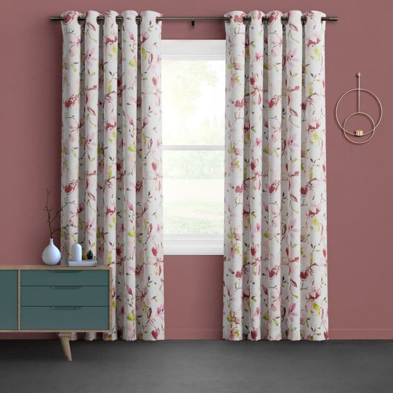 Floral grommet curtains, white with pink-green blossoms, hung on a metal rod and parted to frame a sunlit window, filtering soft daylight in a mauve-walled room with teal dresser.