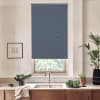 Blue roller blind covers most of window, partially blocking light; mounted above a stainless-steel faucet and sink on a kitchen countertop with wooden cabinets, potted plants, bowl of greens, towel.