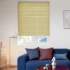 Yellow pleated cellular blind lowered over a window, closed and filtering daylight; small lower pane visible. Context: bright living room with navy sofa, patterned cushions, floor lamp and wall art.