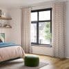 Patterned pleated curtains on a silver rod, full‑length panels with pastel chevron, pulled to frame a black‑framed window and filtering daylight in a bedroom with view of brick houses.