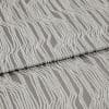Textured grey upholstery fabric with raised white irregular vertical stripes, folded horizontally across the frame; fabric lies flat in a studio close-up with soft, diffuse lighting highlighting its sheen.